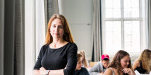 En lärare står i ett klassrum. Bakom henne sitter elever vid sina bänkar.