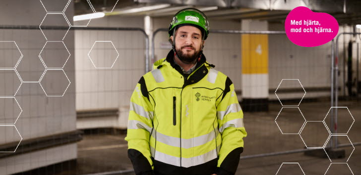 En arbetsmiljöinspektör i skyddskläder och hjälm tittar in i kameran. 